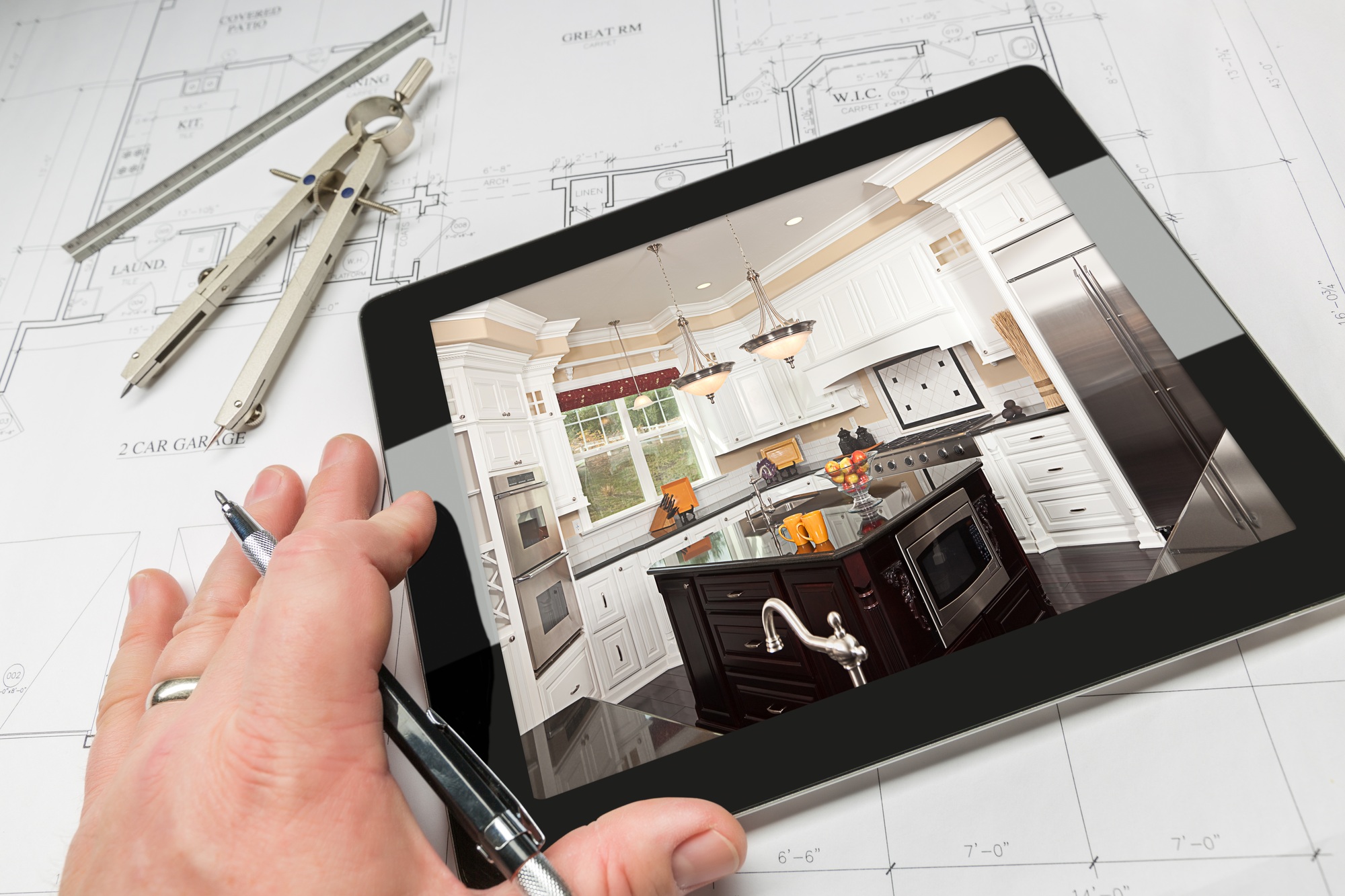 Hand of Architect on Computer Tablet Showing Kitchen Photo Over House Plans